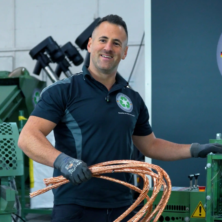 Nico Joannidis in seiner Halle in Heilbronn mit Kupfer-Recyclingmaschinen Mann in schwarzem Poloshirt steht in einer Lagerhalle mit vielen Lichtern.
